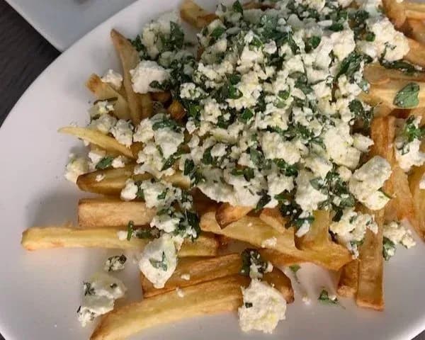 Crispy air-fried fries topped with crumbled feta cheese and fresh chopped parsley on a white plate.