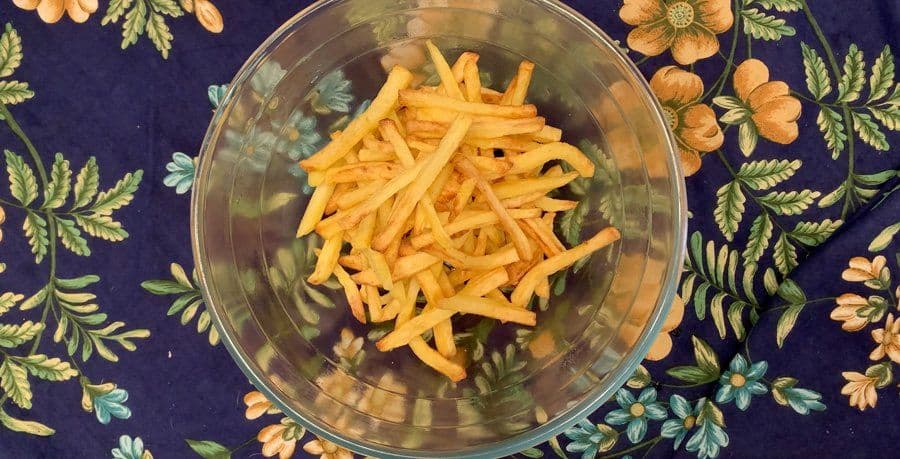 Golden air fryer fries tossed with garlic butter and parmesan cheese in a glass bowl, ready to serve.