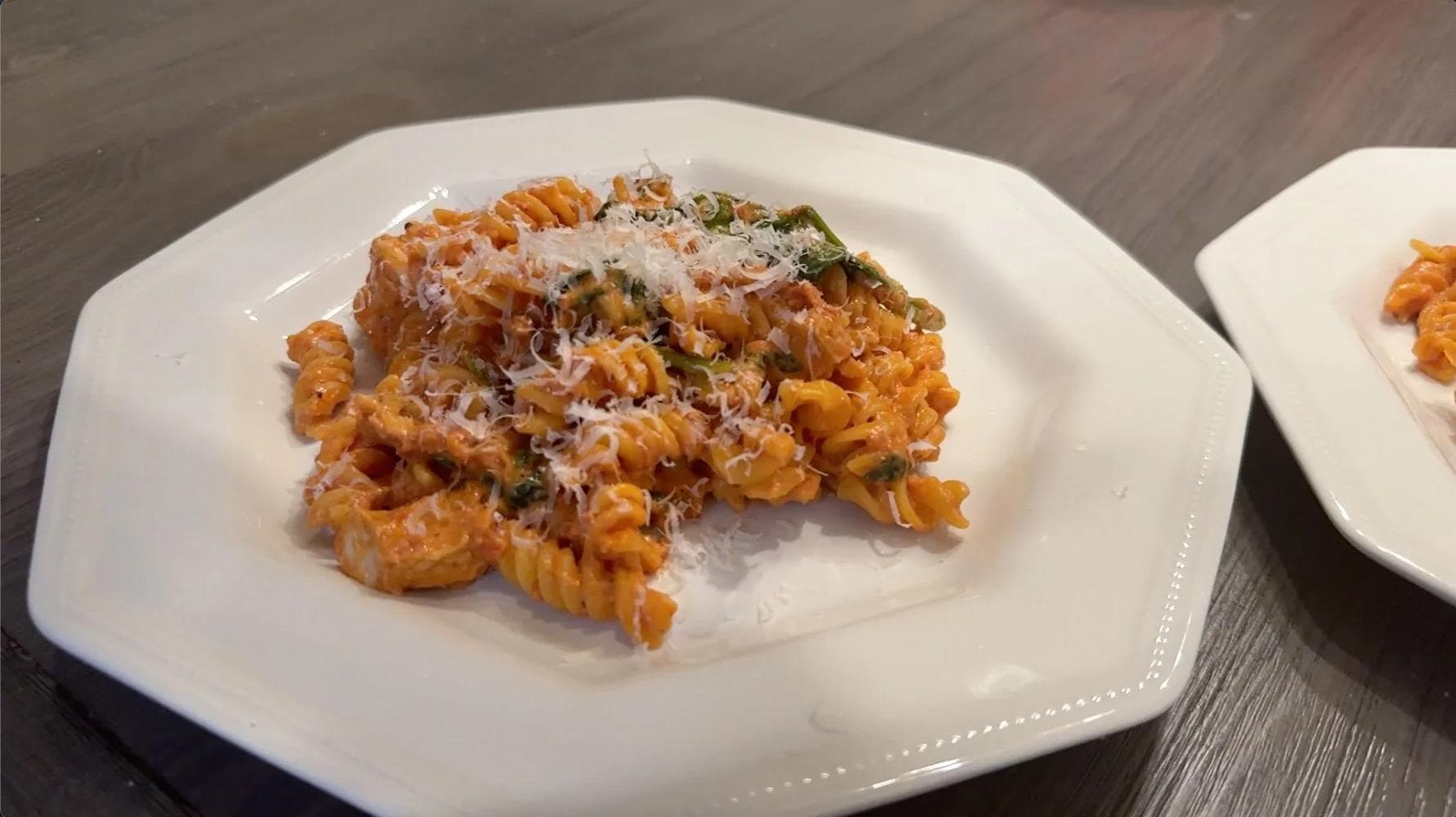 Creamy tomato pasta with rotini noodles, topped with grated cheese and fresh herbs on a white plate.