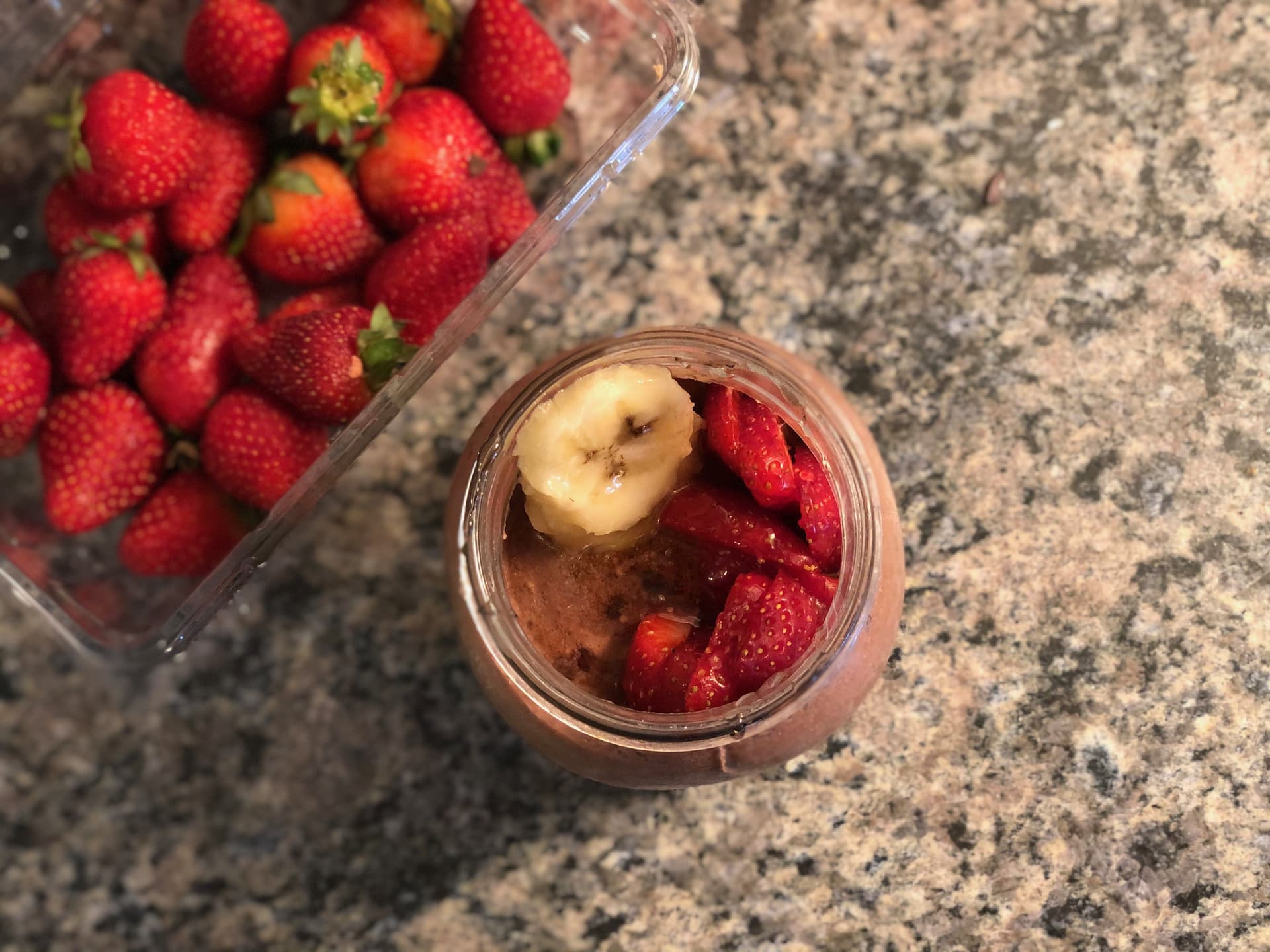 Chocolate banana strawberry overnight oats in a glass jar topped with sliced banana, beside fresh strawberries.