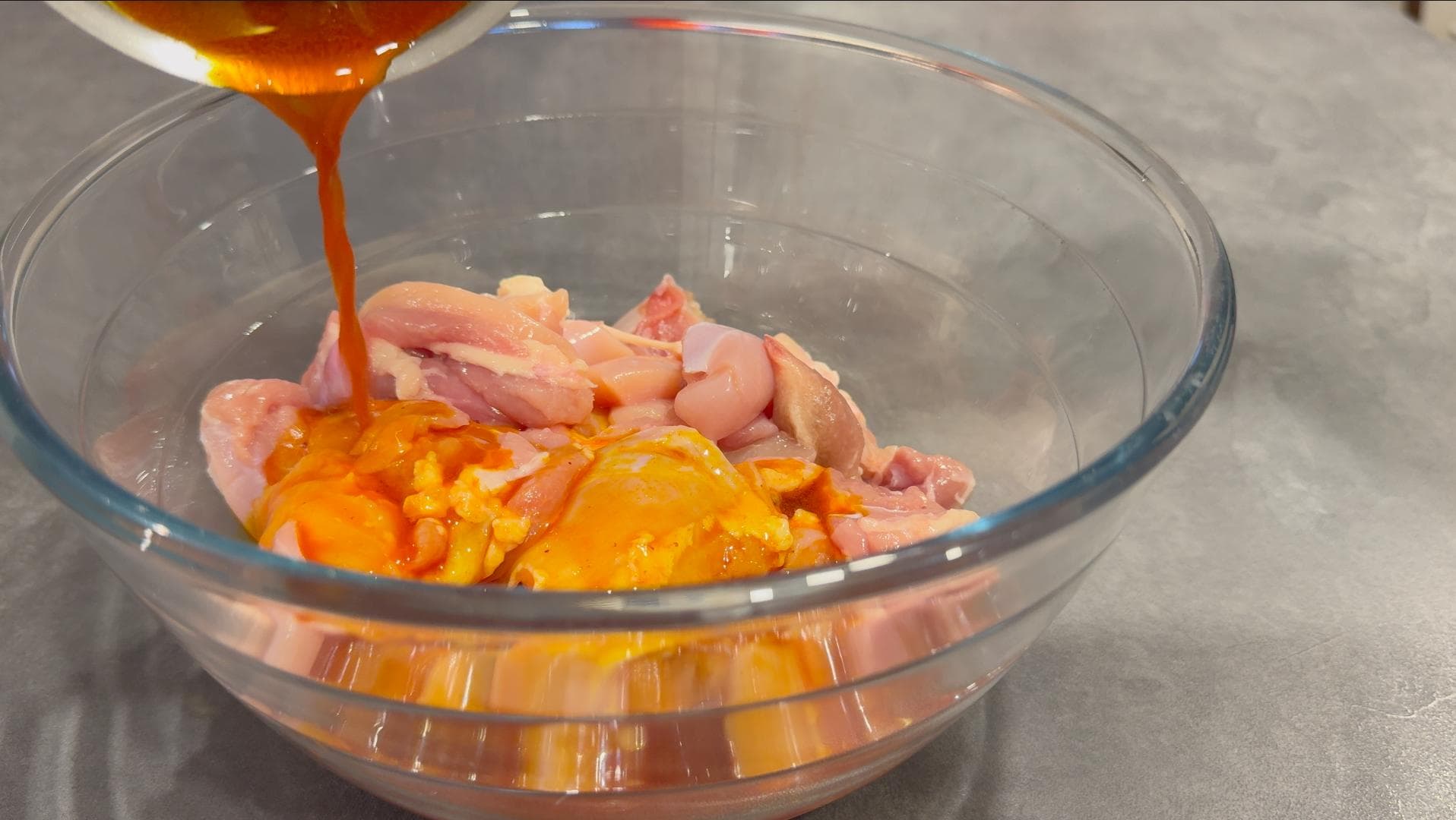 Saffron-infused marinade being poured over raw chicken pieces in a glass bowl for joojeh kebab.