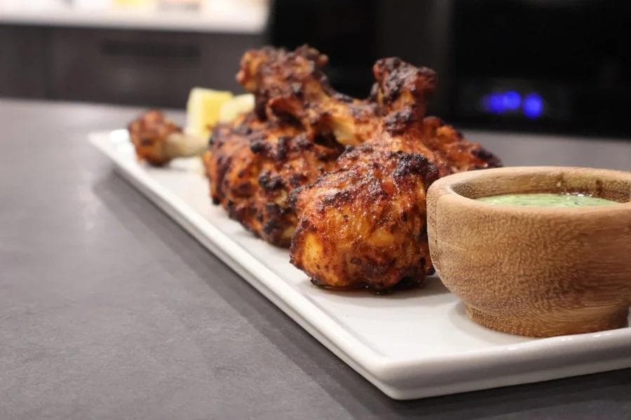Air fryer tandoori chicken pieces with charred, spiced exterior served with green sauce in wooden bowl