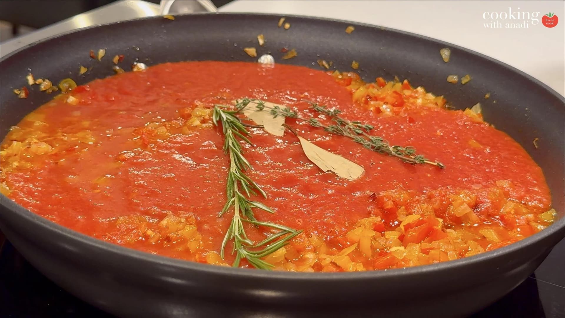 Tomato sauce simmering in a skillet with fresh rosemary sprigs, thyme, and bay leaf over sautéed peppers and onions.