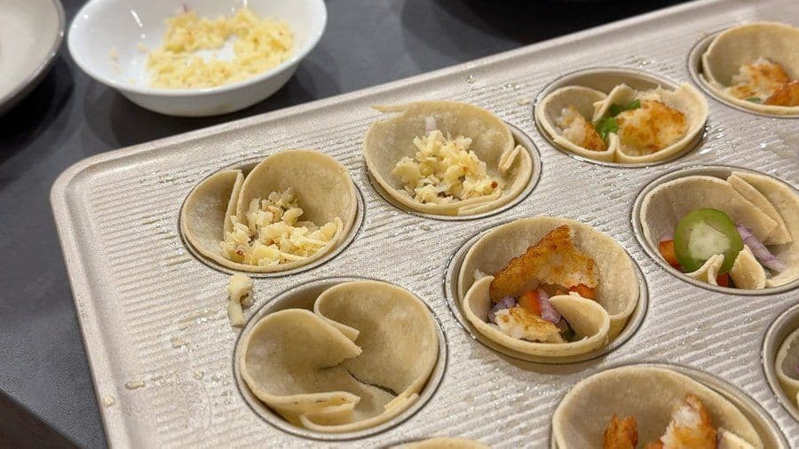 Egg cup muffins in a muffin tin with various vegetarian fillings including cheese, hash browns, and vegetables, some partially filled with egg mixture.