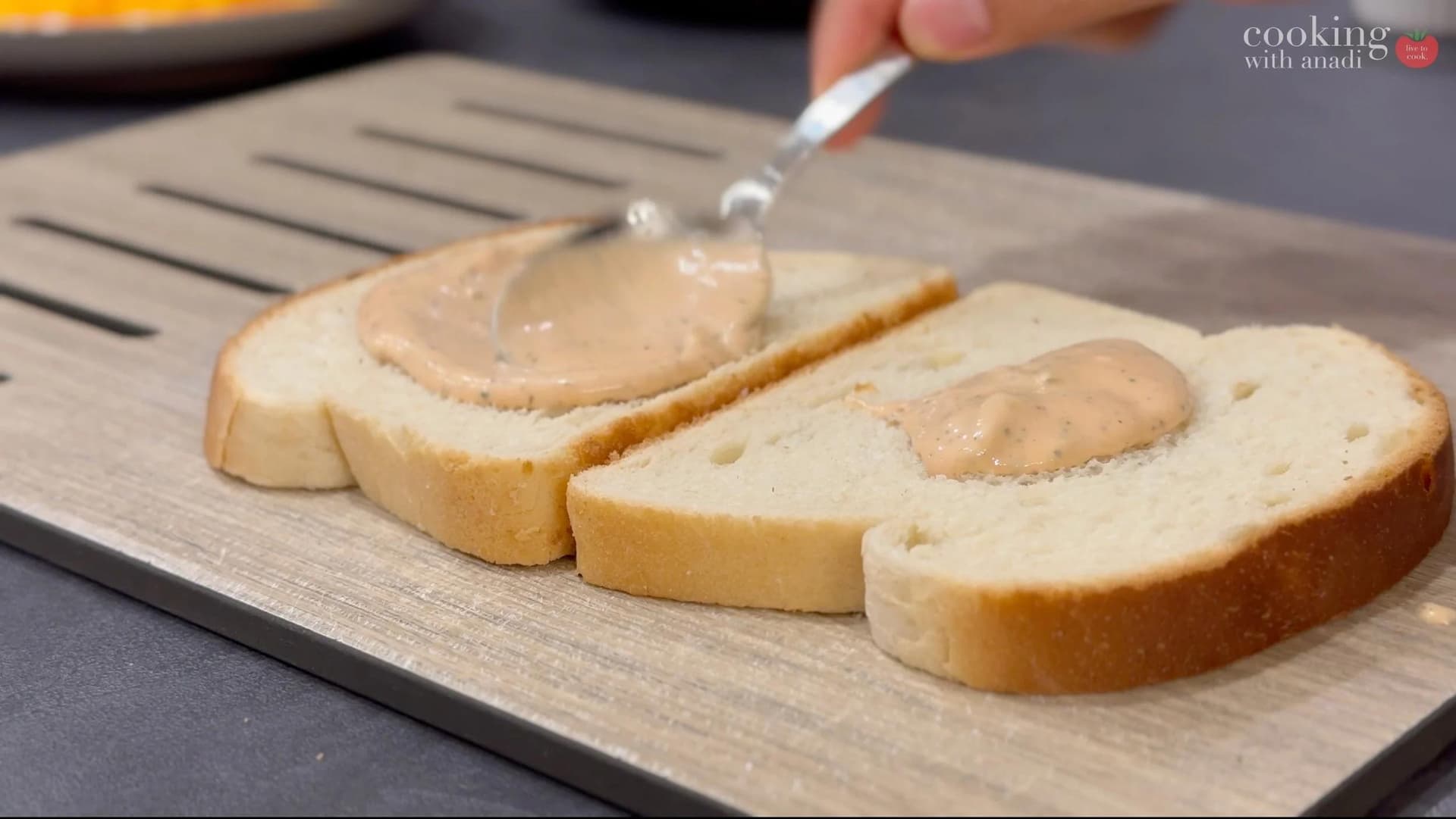 Spreading sauce on sliced bread with a knife on a cutting board for assembling patty melts.