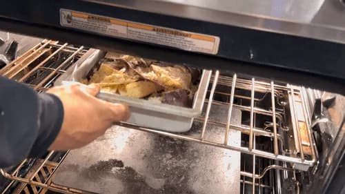 Hand sliding a baking sheet of melted cheese nachos from an oven onto a serving platter.