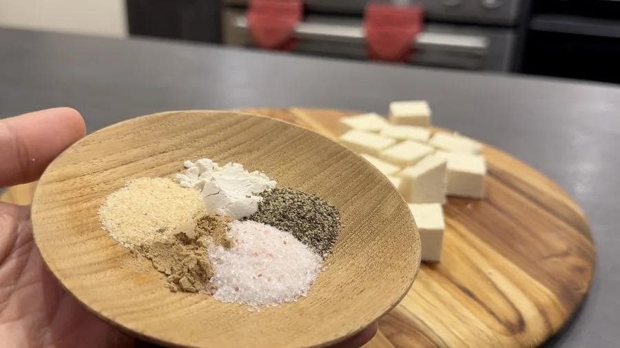Wooden spoon holding dry ingredients for tofu coating: ginger powder, garlic powder, onion powder, salt, pepper, and cornstarch.