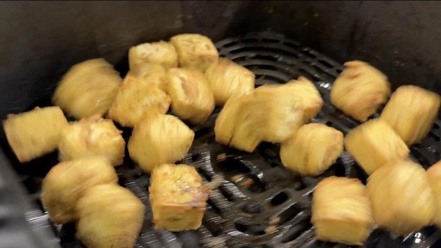 Golden-brown crispy tofu cubes in an air fryer basket halfway through cooking.