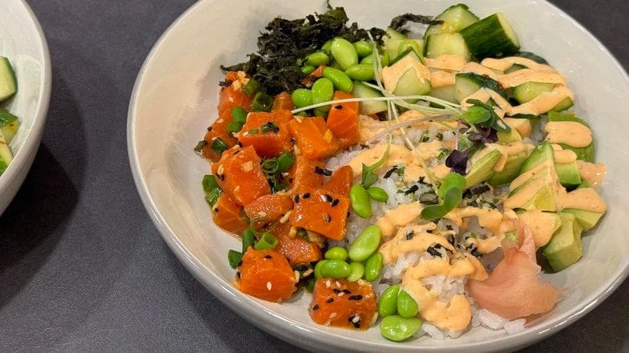 Salmon poke bowl with white rice, raw salmon, avocado, edamame, seaweed, and black sesame seeds.