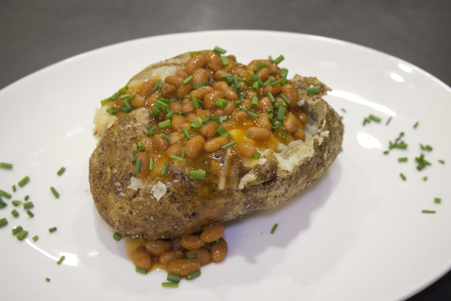 Baked potato topped with baked beans and fresh chives on a white plate