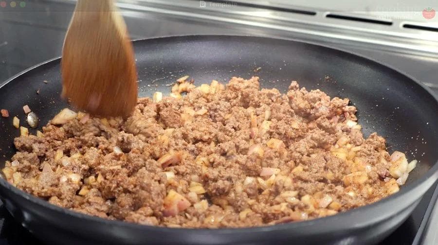 Ground beef being cooked and broken up in a skillet with onions and spices for burrito bowl filling.