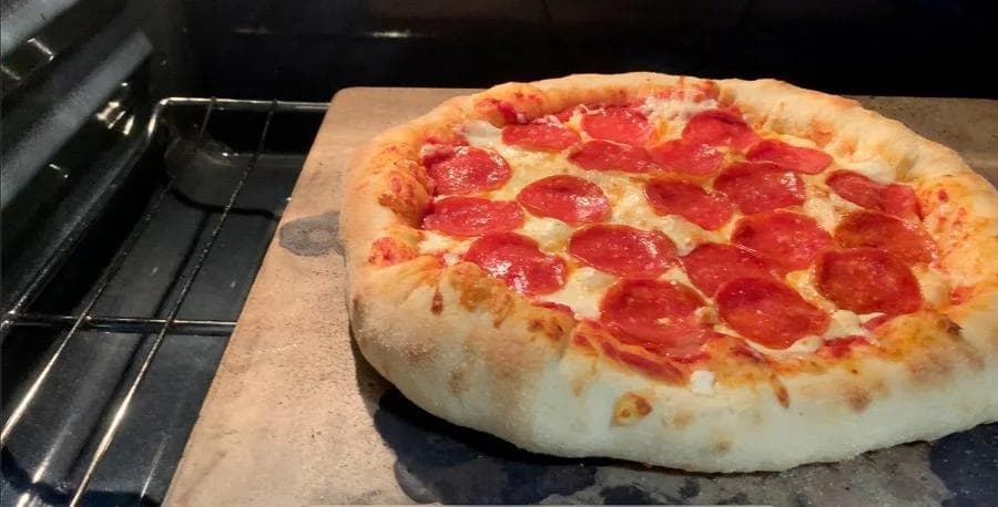 Pepperoni pizza with melted cheese and charred crust on parchment paper inside oven.