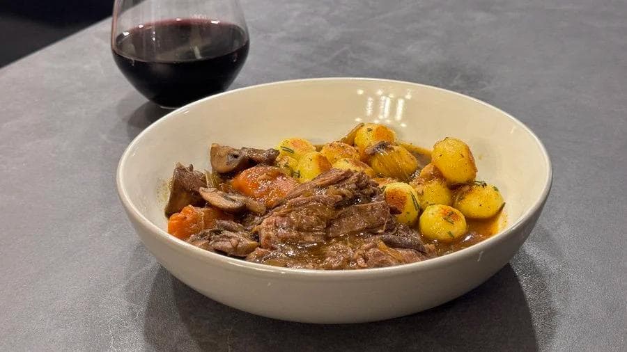 Hearty pot roast with tender beef, roasted potatoes, and carrots served in a white bowl with red wine.
