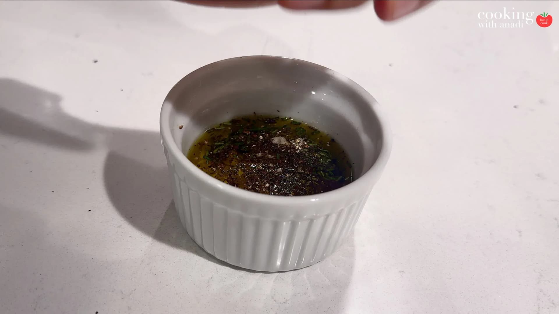 Small white ramekin filled with olive oil, herbs, and freshly ground black pepper, ready to be mixed.