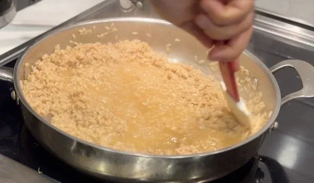 Creamy lobster risotto in a stainless steel pan being stirred with a wooden spoon, showing the creamy, pale yellow rice mixture.