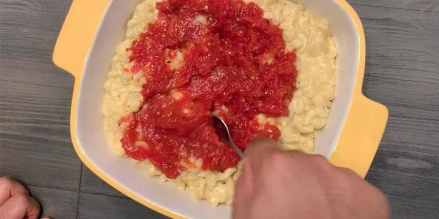 Pizza mac and cheese in yellow casserole dish topped with red tomato sauce being stirred with spoon.