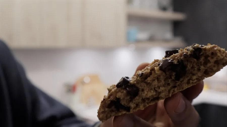 Close-up of a chocolate chip pumpkin cookie held in hand, showing its dense, cake-like texture with dark chocolate chips throughout.
