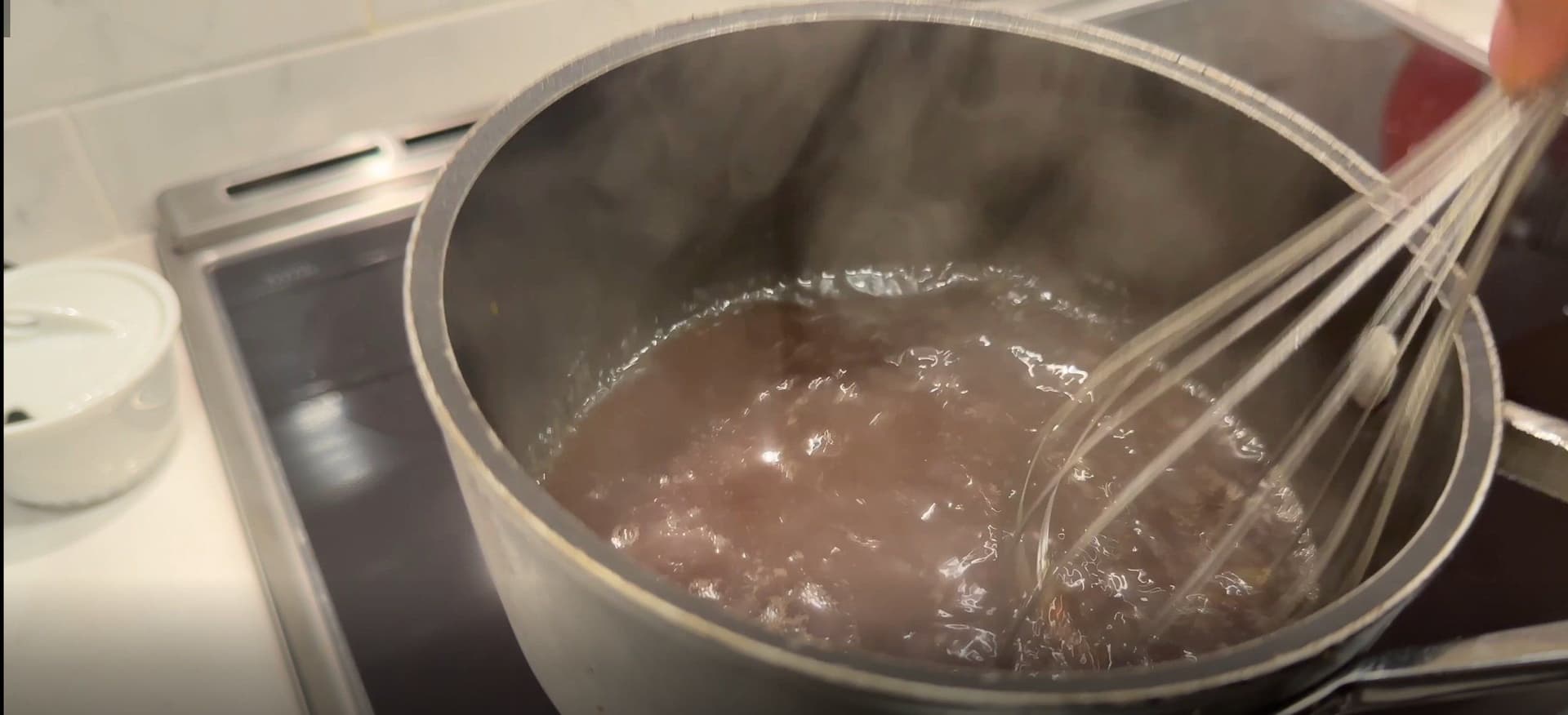 Brown sugar syrup being whisked in a stainless steel pot on a stovetop until dissolved.