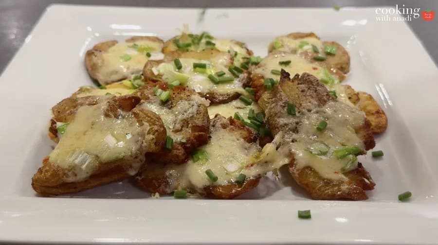 Crispy air fryer smashed potatoes topped with melted cheese and chopped green onions on a white plate.