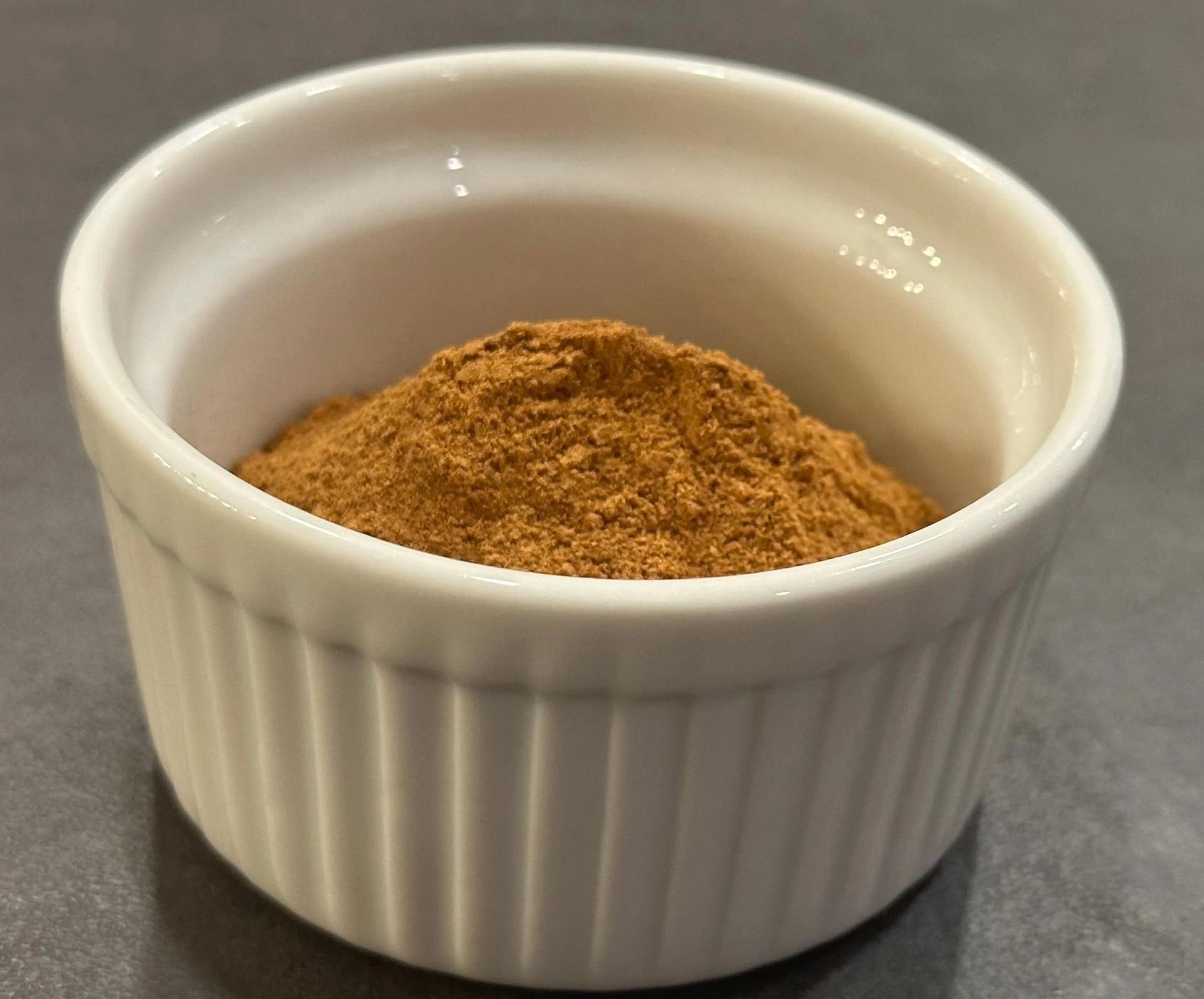 Homemade apple pie spice blend in a white ceramic ramekin on a gray surface.