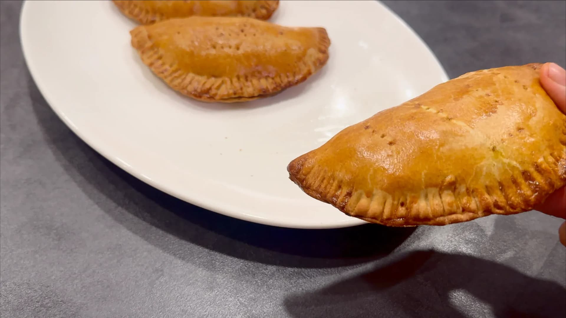 Golden-brown air fryer Nigerian meat pies on a white plate, with one held in hand showing crispy pastry exterior.