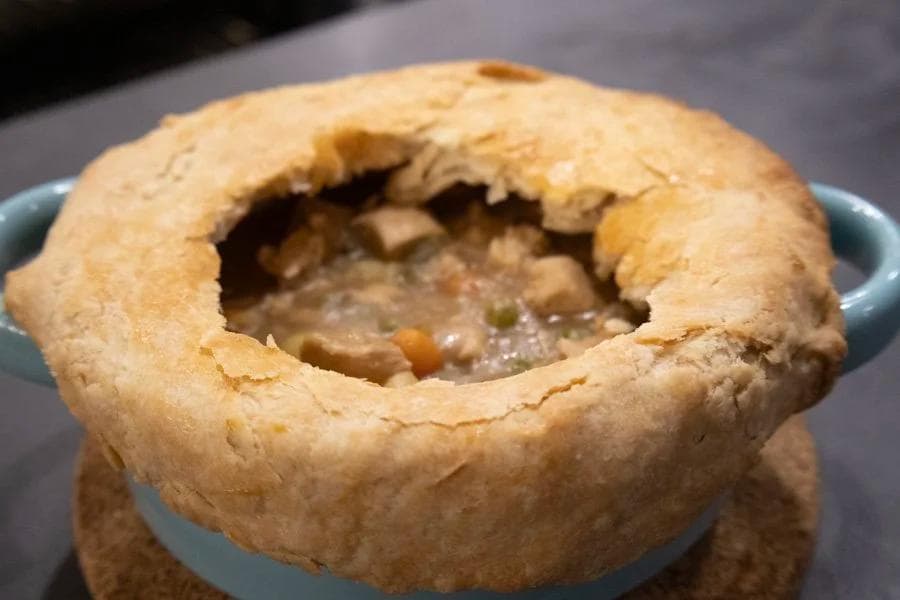 Golden-brown Guinness chicken pot pie in a blue bowl with flaky pastry crust and savory filling visible through opening.