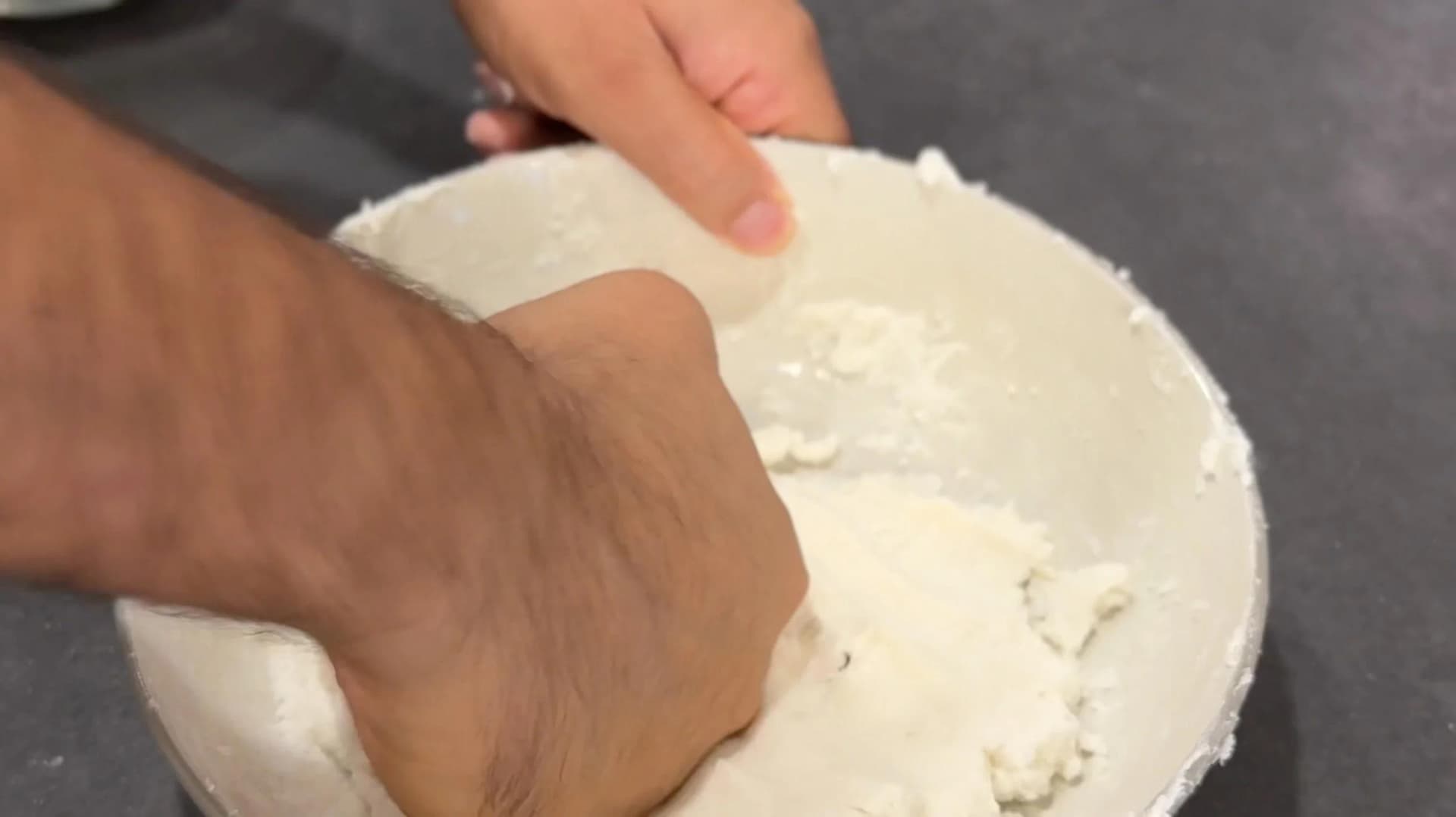Hands kneading smooth white rice dough on a floured surface for making rice noodles.