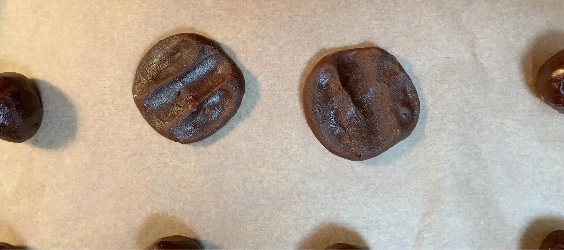 Chocolate s'mores stuffed cookies cooling on parchment paper, showing cracked surfaces and melted filling.