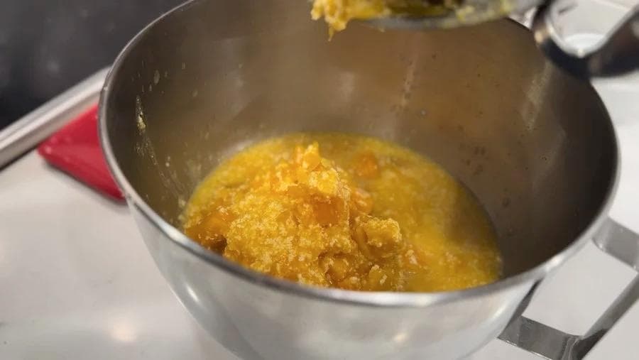 Golden mashed potatoes being mixed in a stainless steel pot on a stovetop.