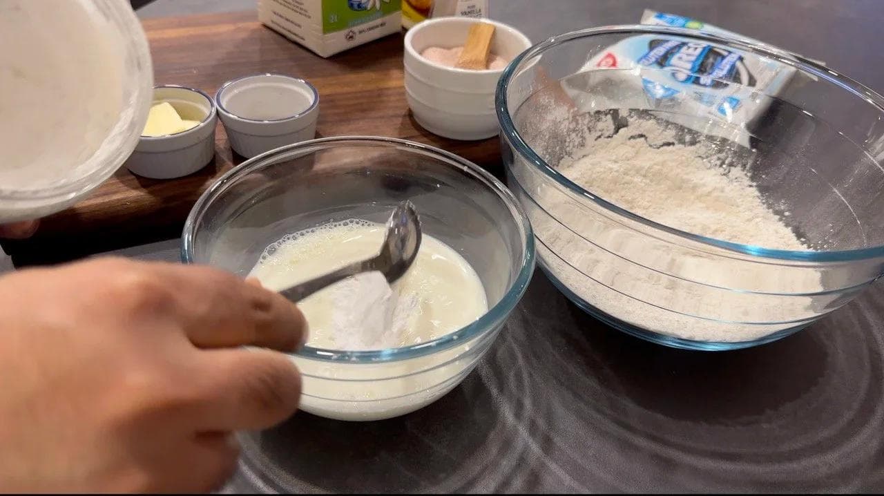 Whisking wet ingredients in a glass bowl next to dry ingredients in another bowl during pancake batter preparation.