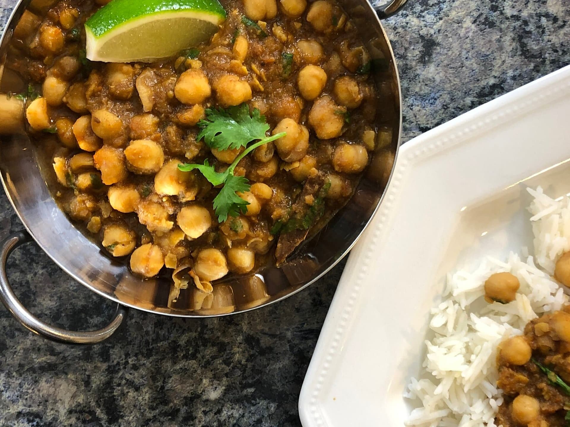 Punjabi chole masala in a steel bowl garnished with cilantro and lime, served alongside rice.