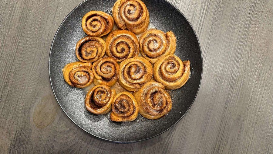 Golden brown crescent roll cinnamon rolls dusted with cinnamon sugar on a dark plate.