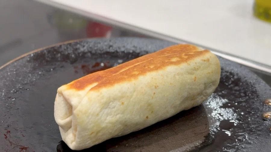 Golden-brown breakfast burrito on a dark plate, toasted on multiple sides until crispy.