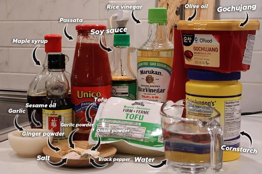 Ingredients for Korean-style air fryer tofu displayed on a kitchen counter, including tofu, soy sauce, gochujang, sesame oil, and various spices.