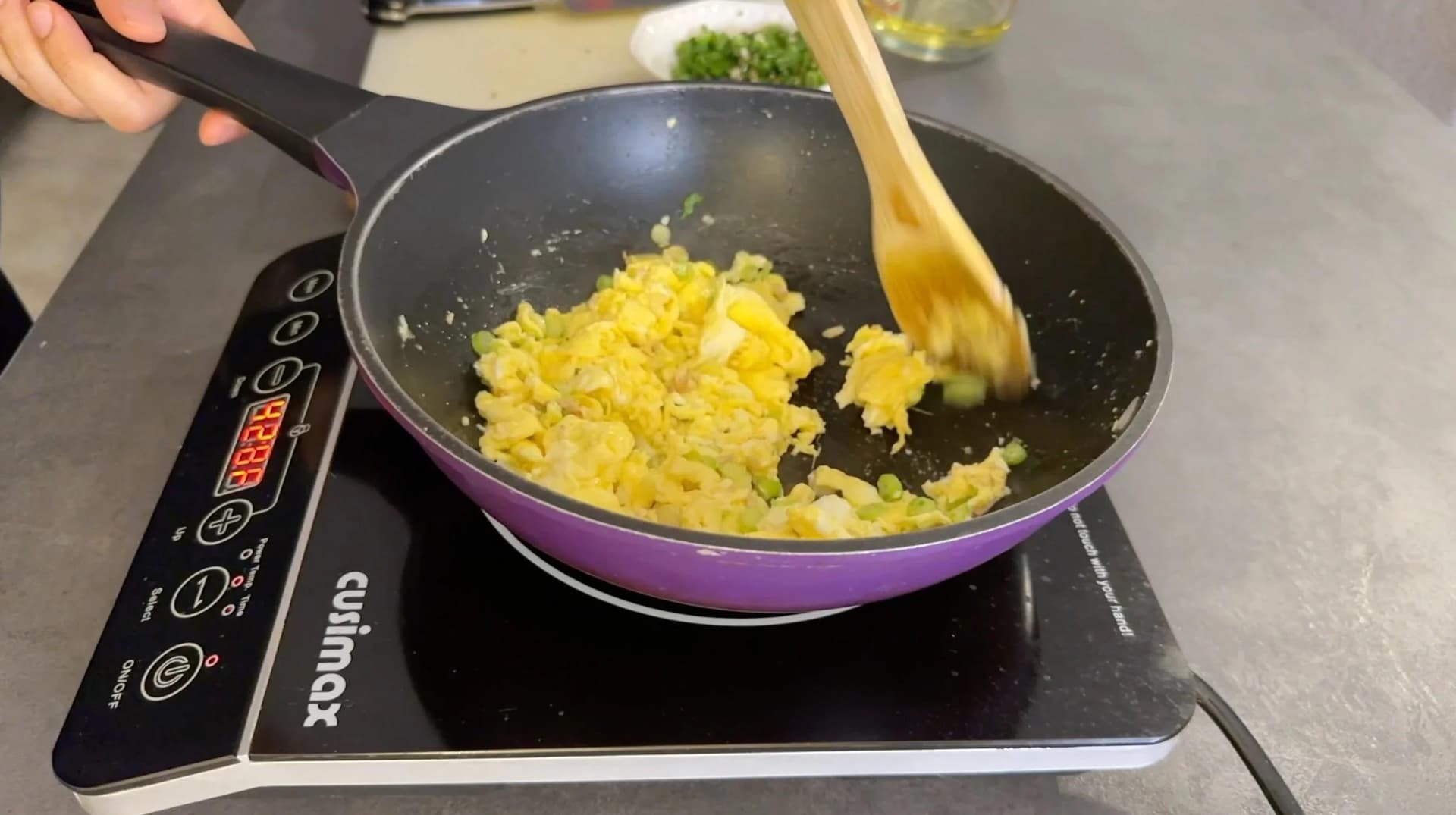 Scrambled eggs and rice being stirred together in a purple wok with a wooden spatula on an induction cooktop.