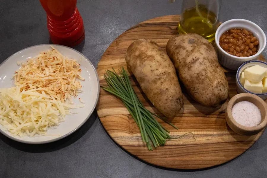 Ingredients for jacket potatoes: two russet potatoes, shredded cheddar and mozzarella cheese, baked beans, butter, chives, and seasonings.