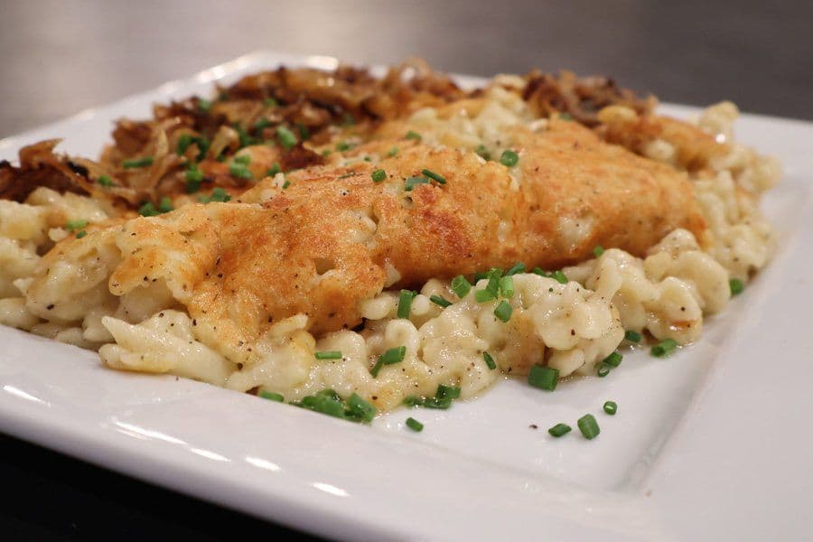 Käsespätzle plated on white dish with melted cheese, crispy fried onions, and fresh chives garnish.