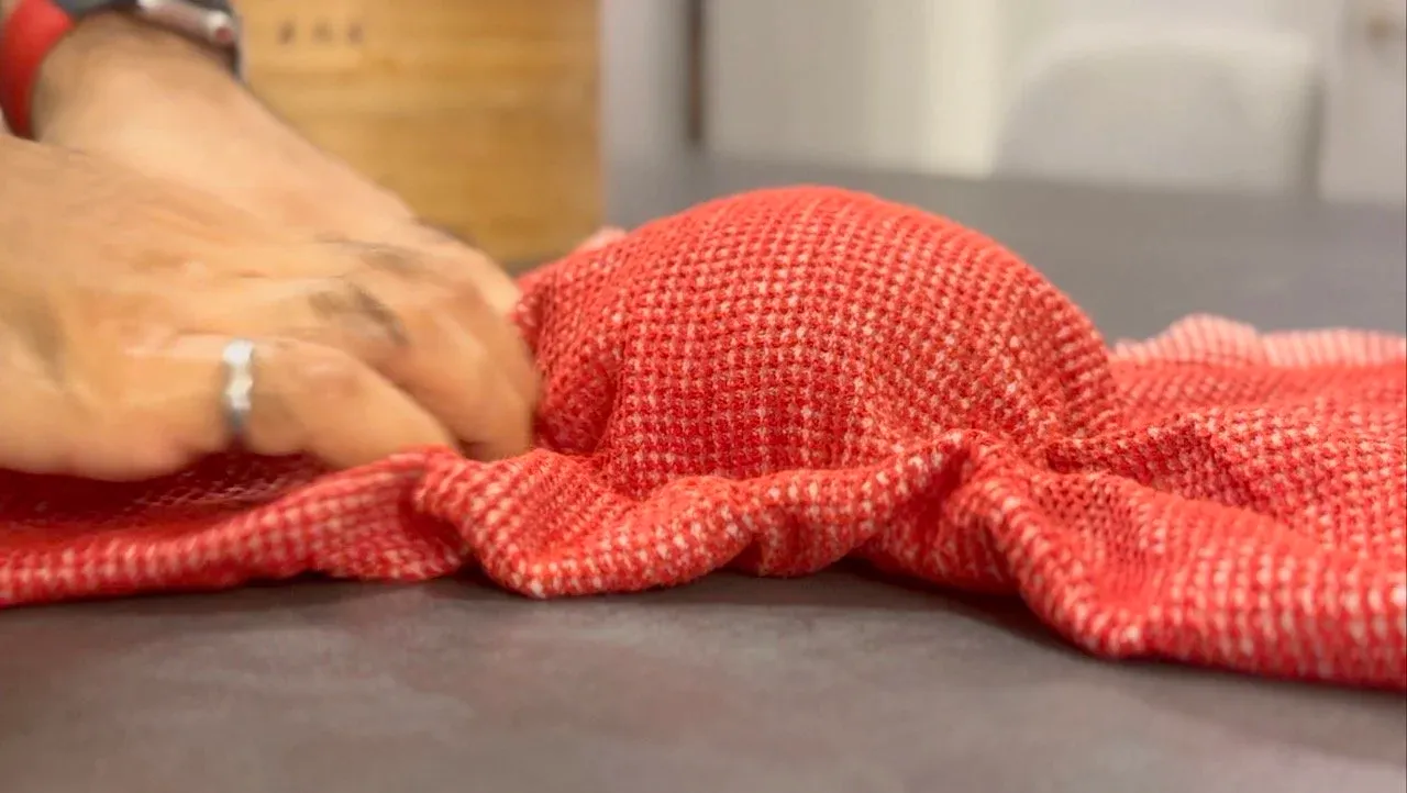 Red cloth covering a dough ball on a work surface with a hand resting on top.