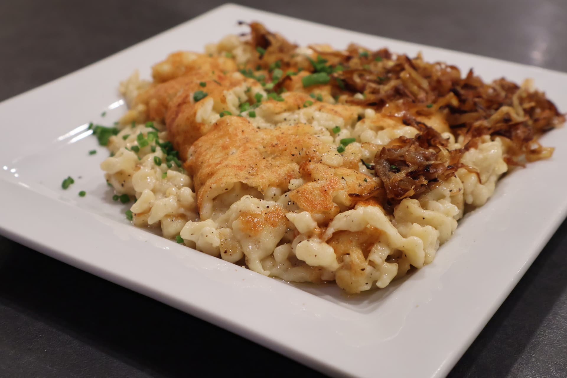 Käsespätzle served on a white plate with crispy fried onions, melted cheese, and fresh chives.