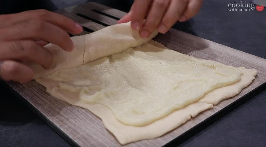 Spreading mashed potatoes evenly over unrolled crescent roll dough, leaving a border around the edges.