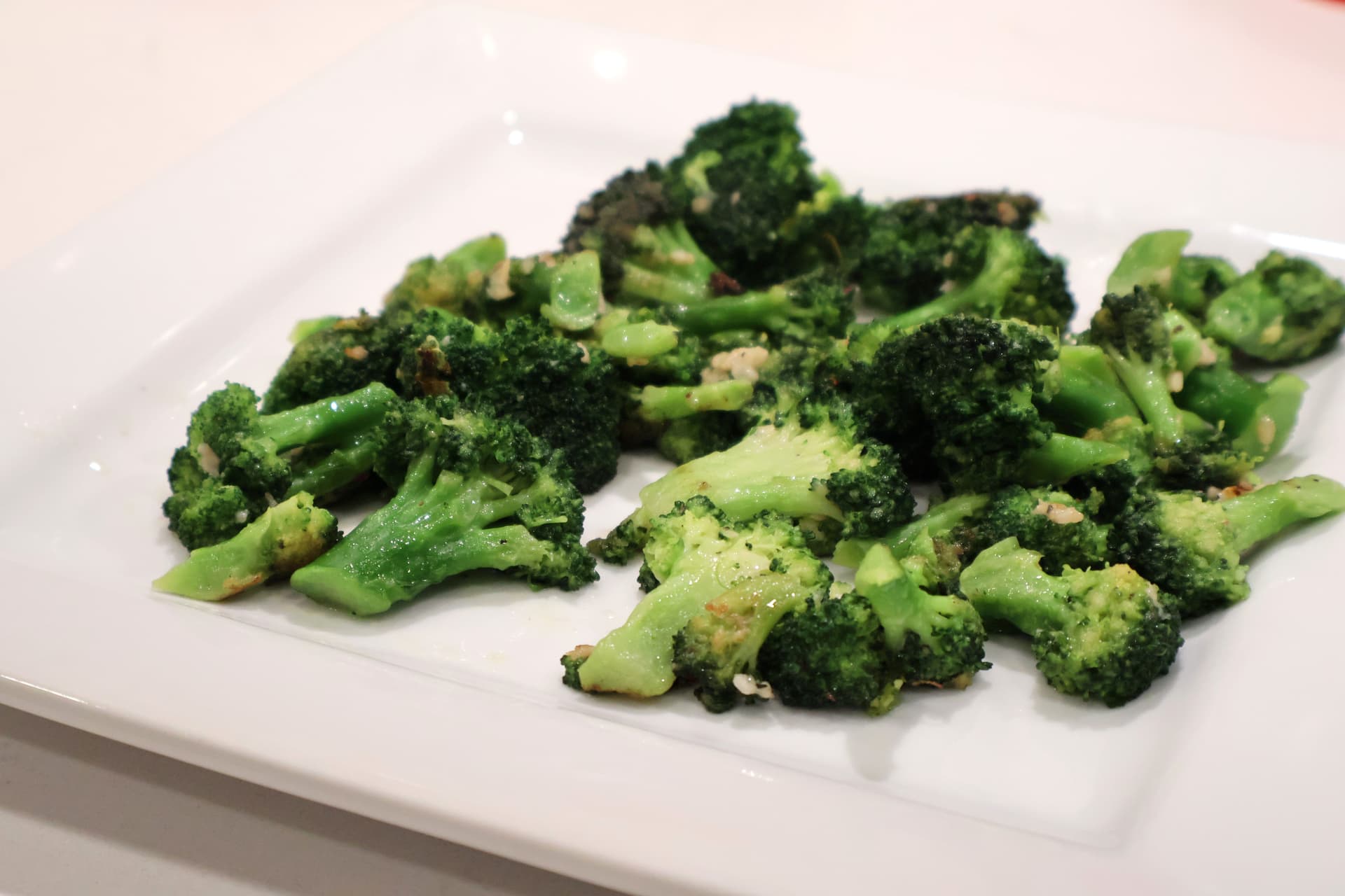 Roasted broccoli florets with garlic butter and seasoning on a white plate.