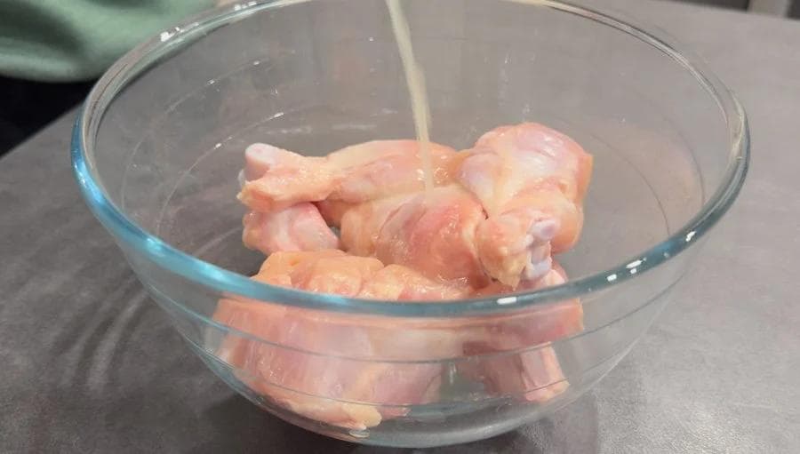 Raw chicken drumsticks marinating in lemon juice and spices in a glass bowl during first marinade stage.