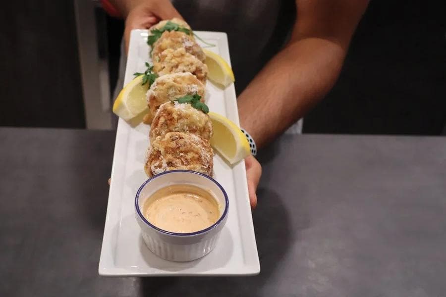 Perkedel Daging Kentang served on a white rectangular plate with lemon wedges and a creamy dipping sauce in a small bowl.