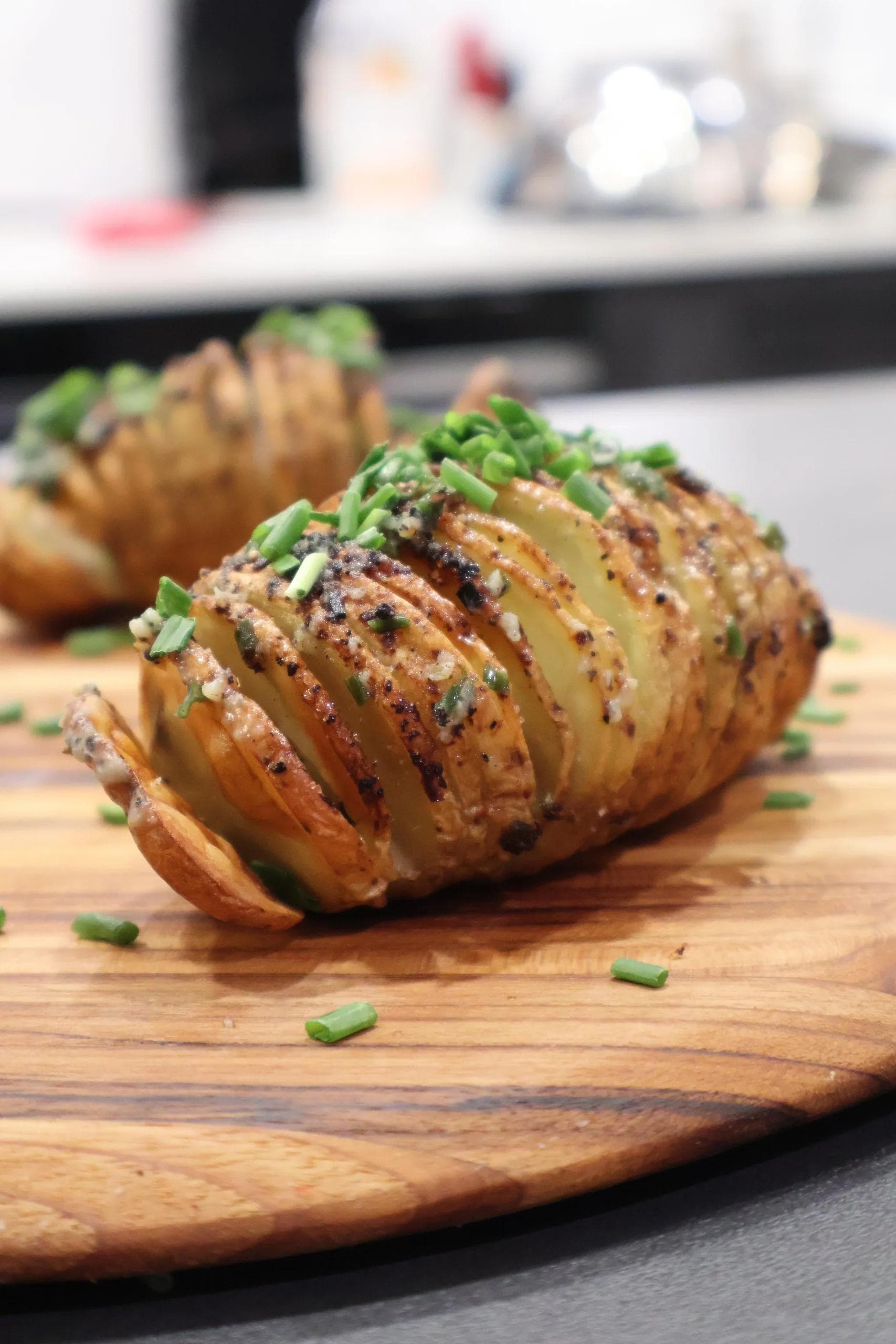 Crispy air fryer hasselback potatoes with golden-brown sliced exterior and fresh chives on a wooden board.