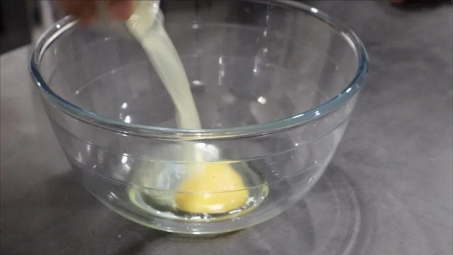 Wet ingredients being mixed in a glass bowl with a spatula, including egg and yellow liquid.