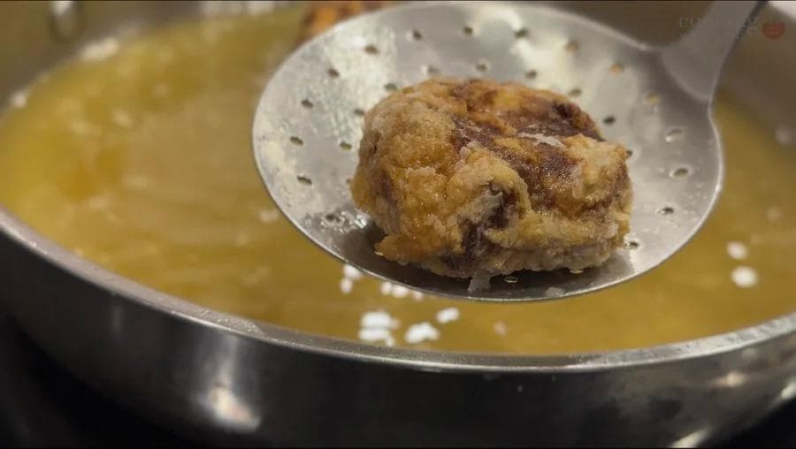 Golden-brown perkedel being lifted from hot oil with a slotted spoon during frying.