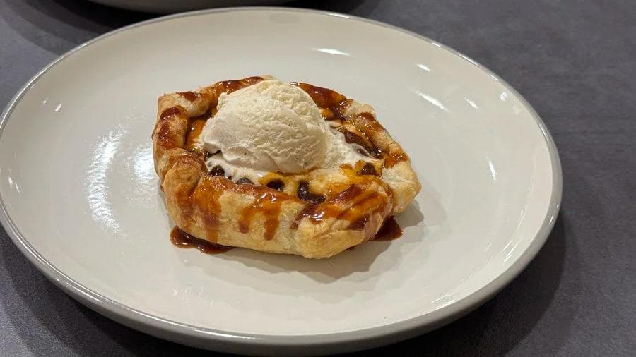 Mini puff pastry apple pie topped with vanilla ice cream on a white plate.