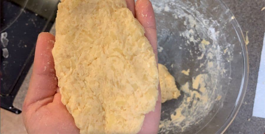 Hand holding an oblong-shaped potato and corn flour mixture ready to fry for hash browns.