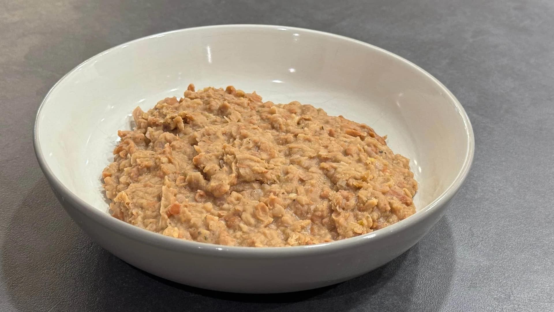 Homemade refried beans in a white bowl with a thick, creamy texture and light brown color