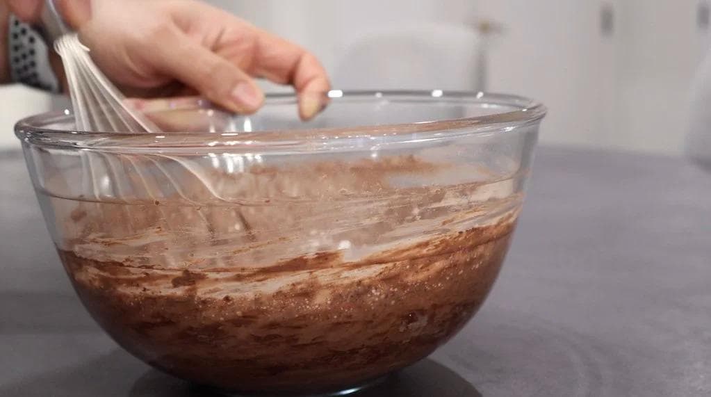 Whisking heavy cream, cocoa powder, sugar, and vanilla in a glass bowl until soft peaks form.